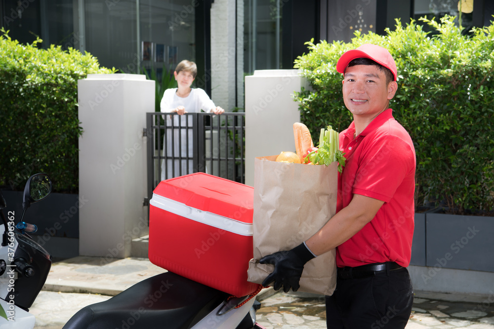 身穿红色制服的亚洲送货员将一袋食品、水果、蔬菜和饮料送到w