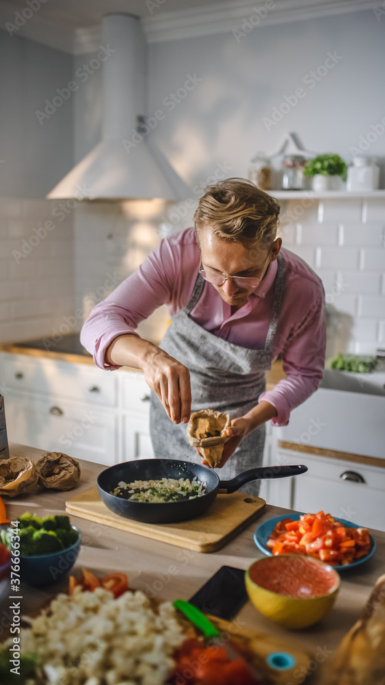 英俊的年轻人在煎锅上准备健康的素食。撒健康的绿色食物