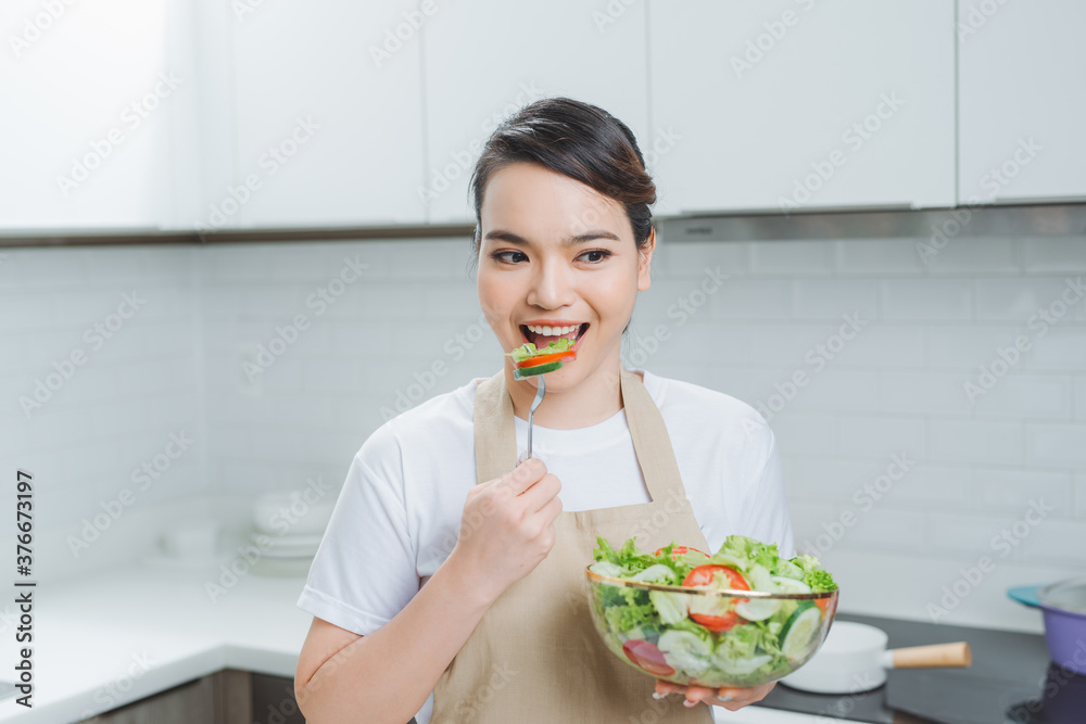 年轻女子在厨房里吃混合沙拉。