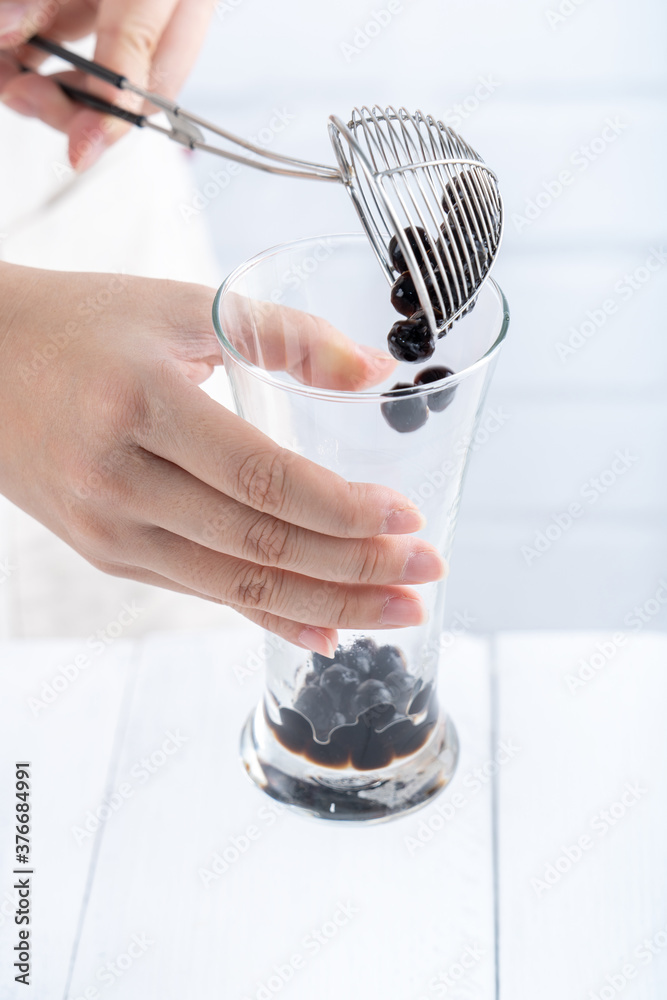 Making bubble tea, scoop and pour cooked brown sugar flavor tapioca pearl bubble balls into cup on w