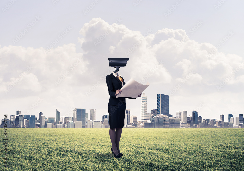 Camera headed woman standing on green grass against modern cityscape