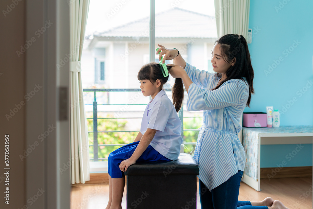 Asian Mother is combing her daughters hair on the morning before going to school in living room at 