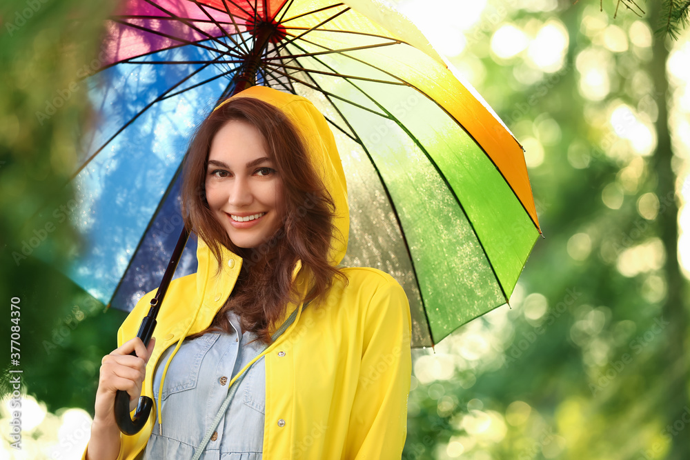 美丽的年轻女子在公园里打着雨伞，穿着雨衣