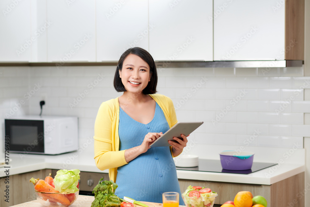 孕妇在室内通过便携式电脑准备健康膳食和搜索纯素食食谱。