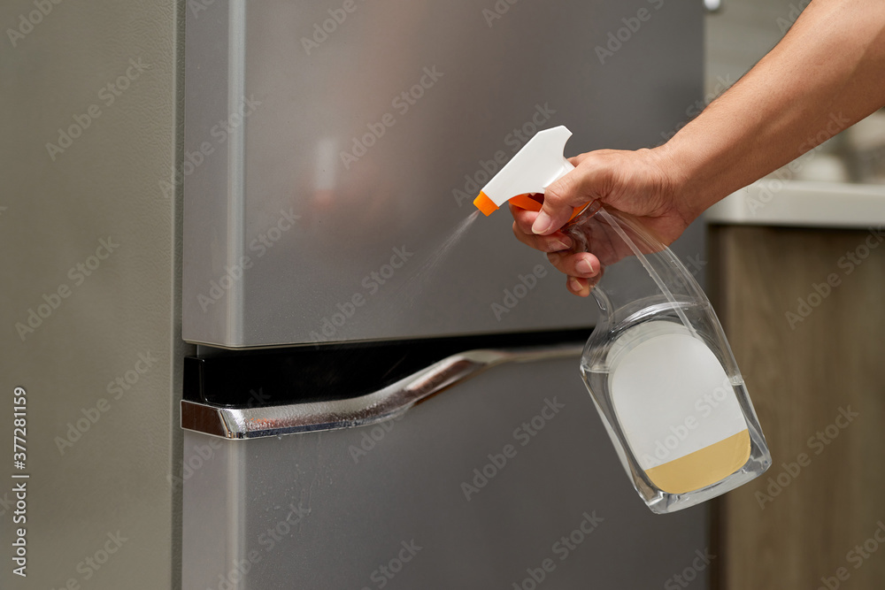 Hand hold bottle alcohol spraying the handle of the fridge door.