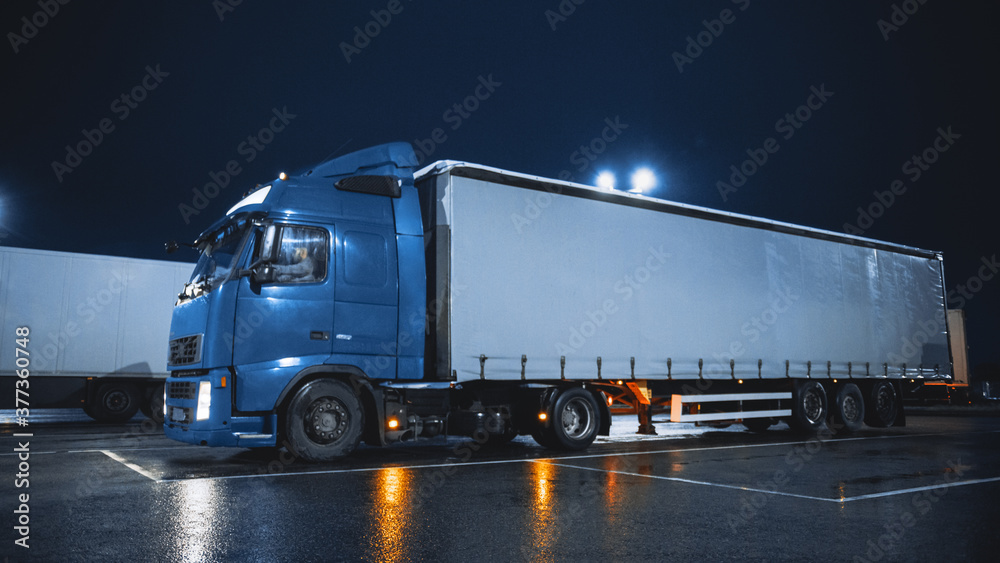 Blue Semi-Truck with Cargo Trailer Drives On Overnight Parking Space where Other Trucks are Standing