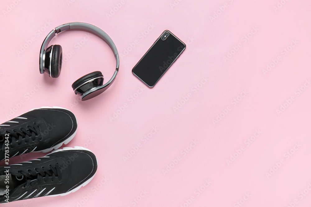 Sportive shoes, mobile phone and headphones on color background