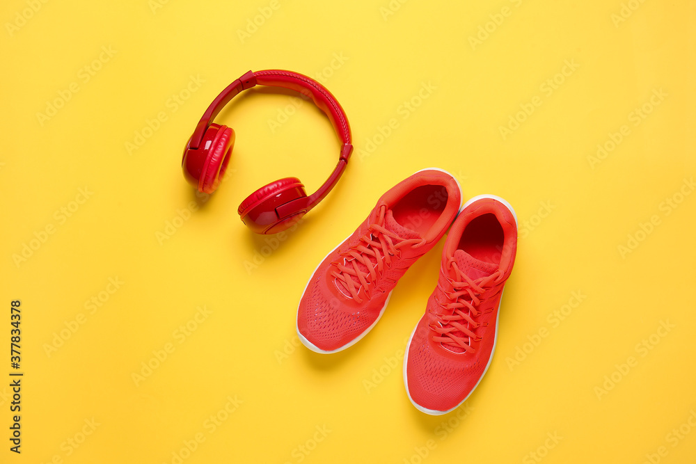 Sportive shoes and headphones on color background