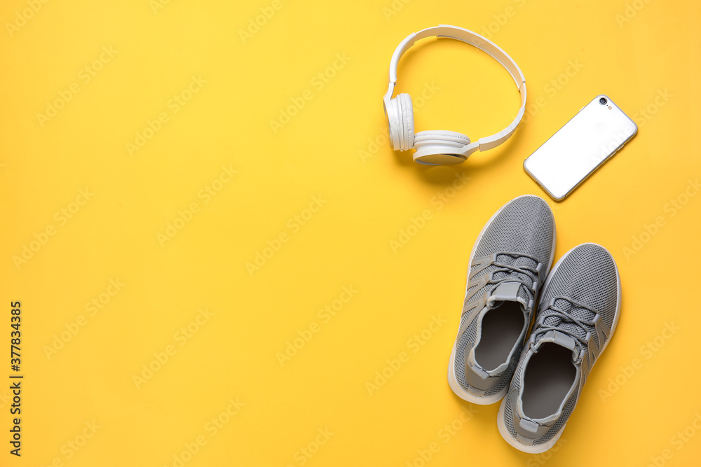 Sportive shoes, mobile phone and headphones on color background