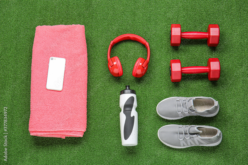 Sportive shoes, towel, dumbbells, bottle of water, mobile phone and headphones on color background