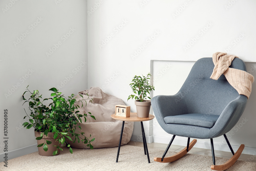 Interior of room with stylish armchair and houseplants near white wall