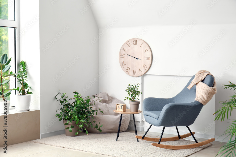 Interior of room with stylish armchair and houseplants near white wall