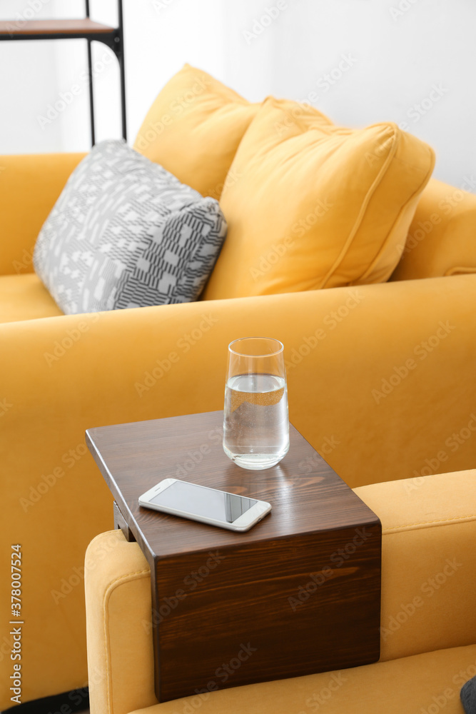 Glass of water and mobile phone on armrest table in room