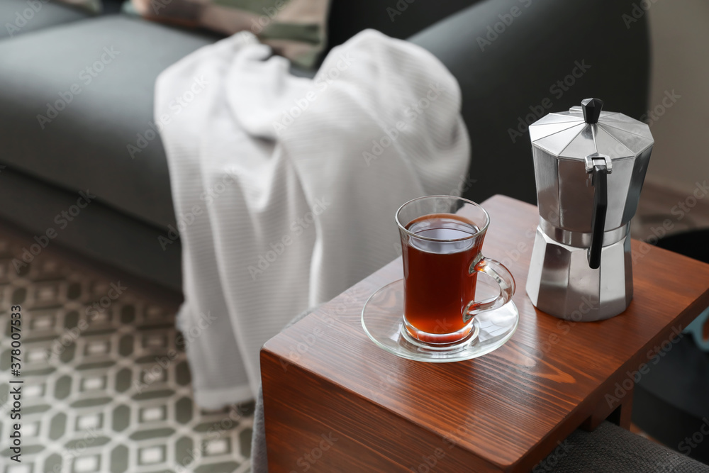 Cup of drink and coffee pot on armrest table in room