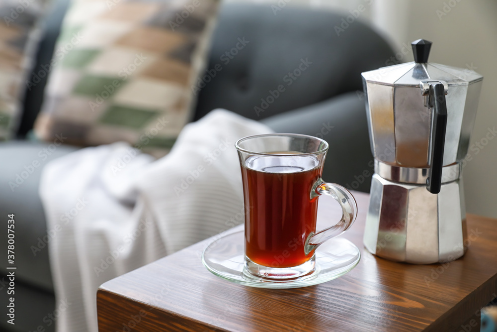 Cup of drink and coffee pot on armrest table in room