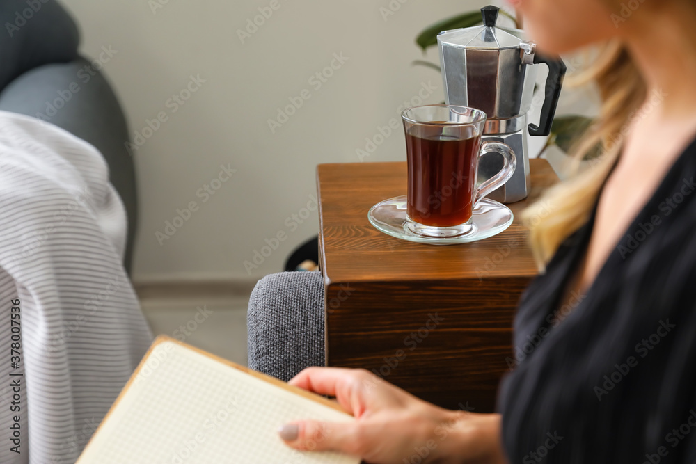 Woman with cup of coffee reading book on sofa at home