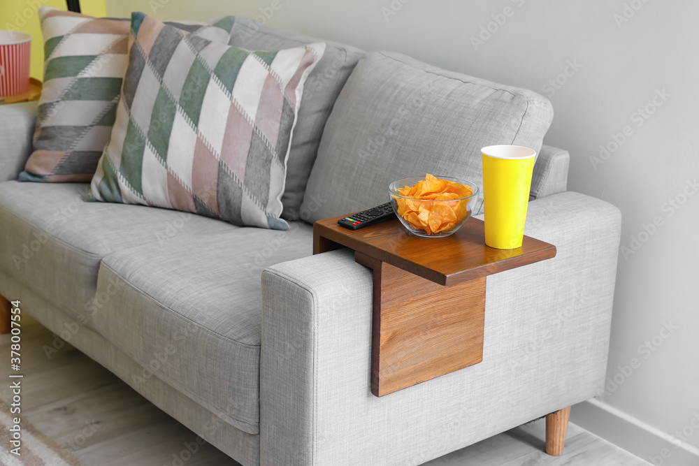 Bowl with chips and remote control on armrest table in room