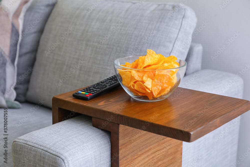 Bowl with chips and remote control on armrest table in room