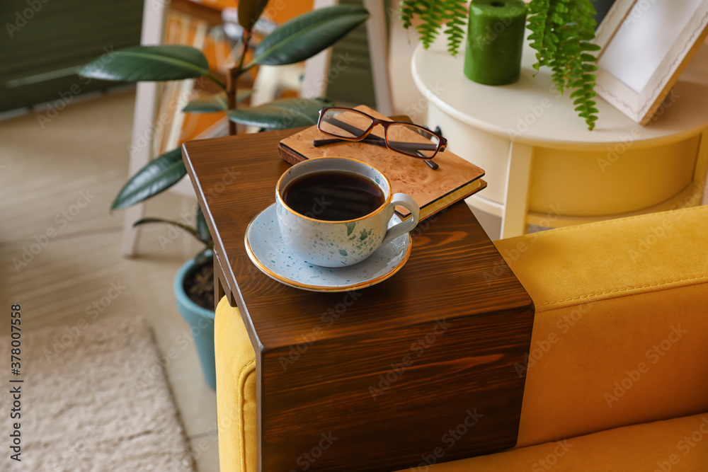 Cup of tea with book on armrest table in room