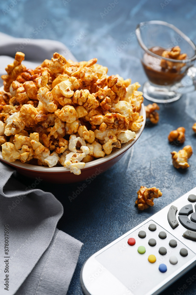 Caramel popcorn with remote control on color background