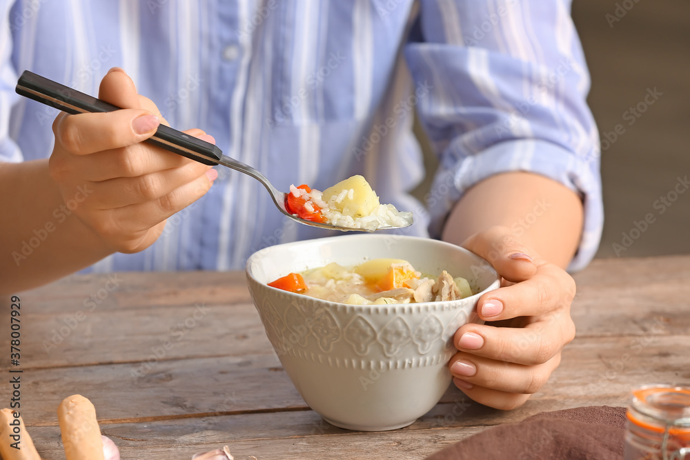 Woman eating tasty rice soup at table