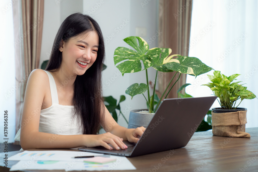 Asian girl typing data to her computer notebook for prepare her report on the wooden deak with the g