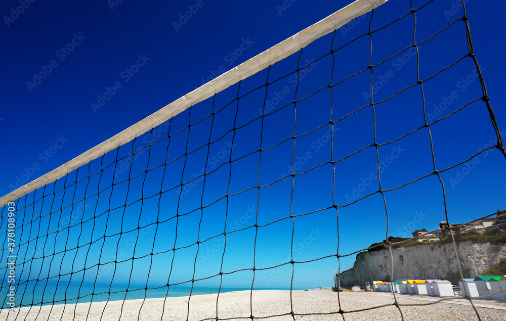 Close-up view of a volleyball net over clean sand beach and ocean background with blue sky