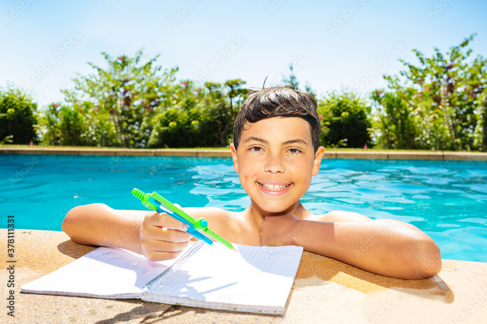 Little boy in swimming pool doing homework holding compass on the border smile and looking at camera