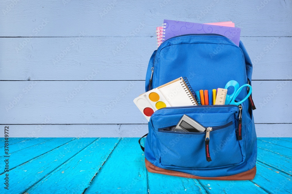 Classic school backpack with colorful school supplies and books on desk.