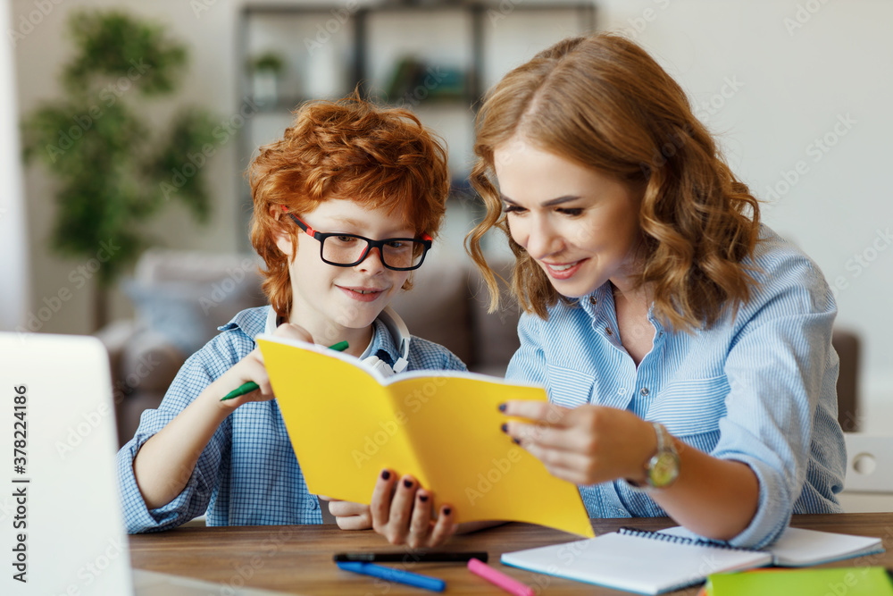 Mother helping child with homework, looks at her sons notebook at home.