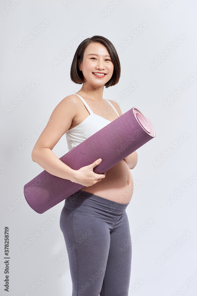 Joyful pregnant woman holding yoga mat smiling to camera posing over white background. Pregnant life