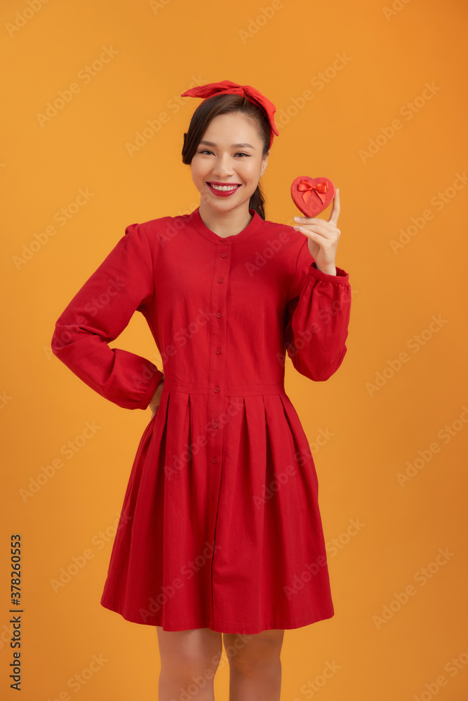 Portrait of a happy pretty asian woman holding present box while standing and looking at camera isol