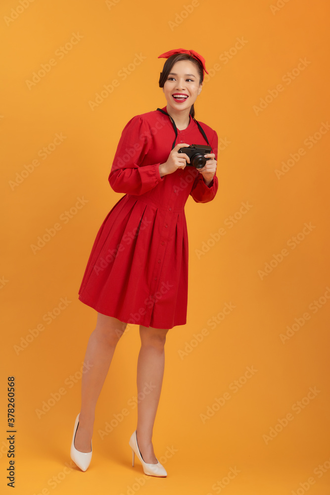 Smiling young Asian girl holding photo camera isolated on a orange background