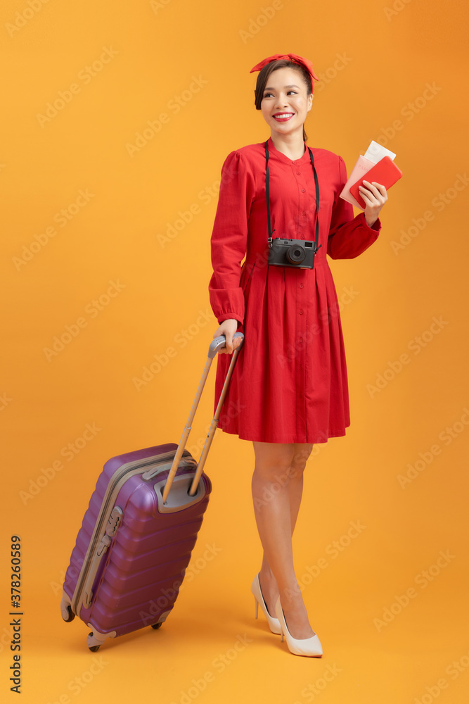 Beautiful young woman smiling and pulling luggage isolated on orange background