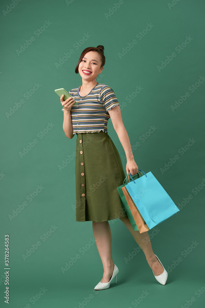 Full length portrait of a happy young woman holding shopping bags and mobile phone