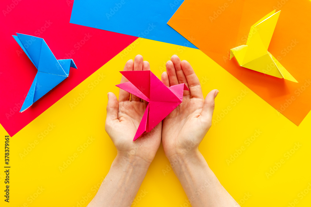 Origami bird in female hands. Care peace concept. Top view