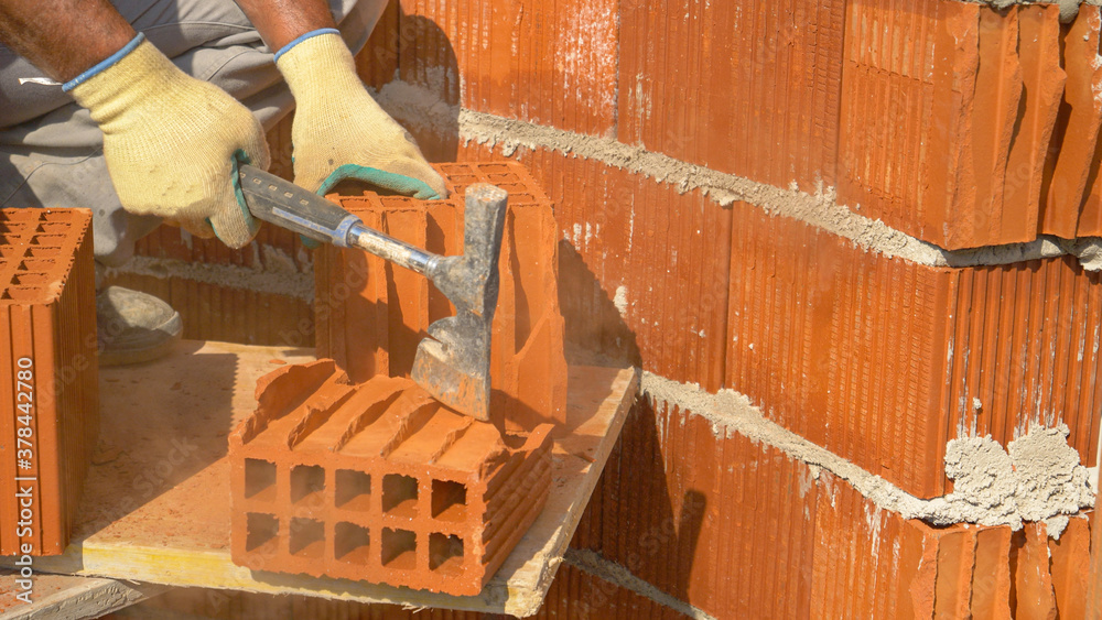 CLOSE UP: Unrecognizable male bricklayer uses an axe to cut a brick in half.