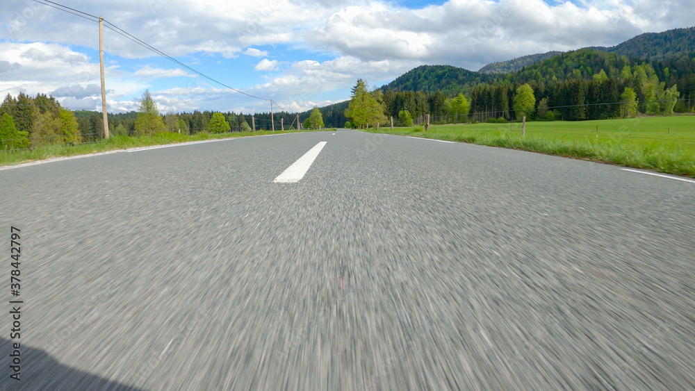 POV: Speeding down empty road crossing a beautiful green valley on a sunny day.