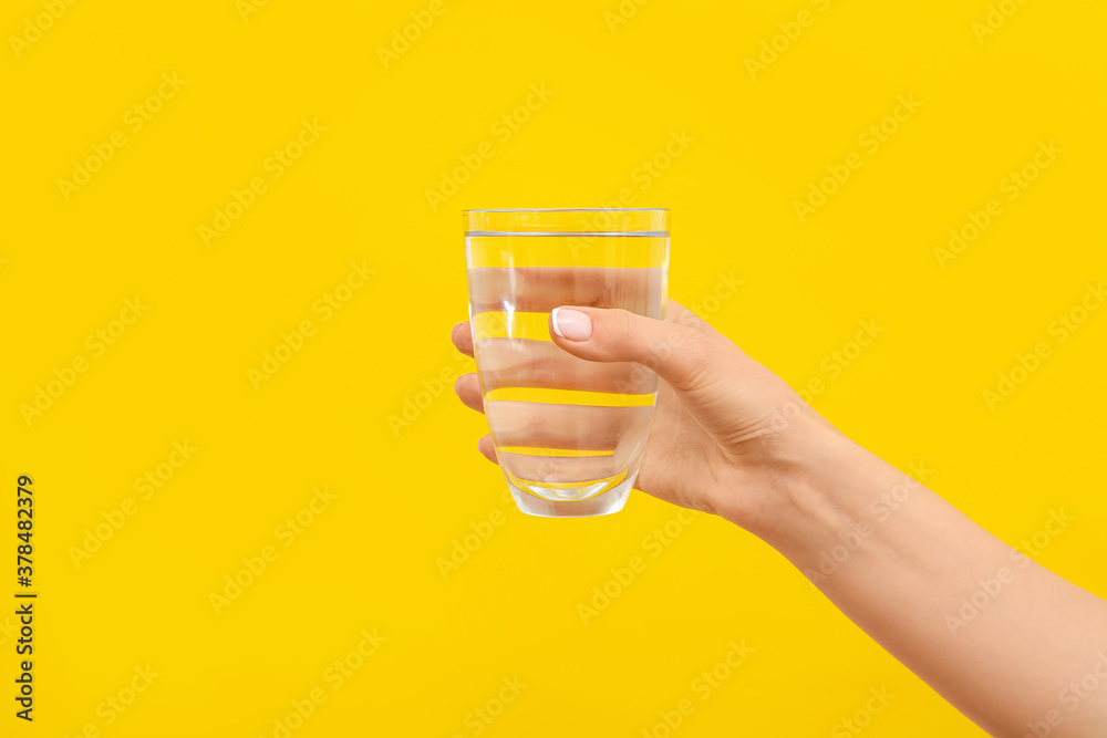 Hand with glass of water on color background