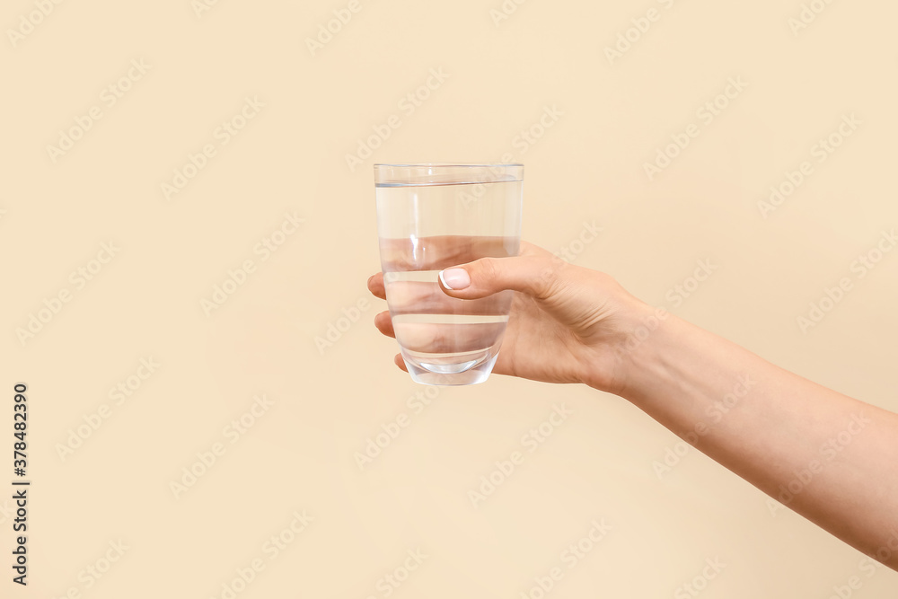 Hand with glass of water on color background