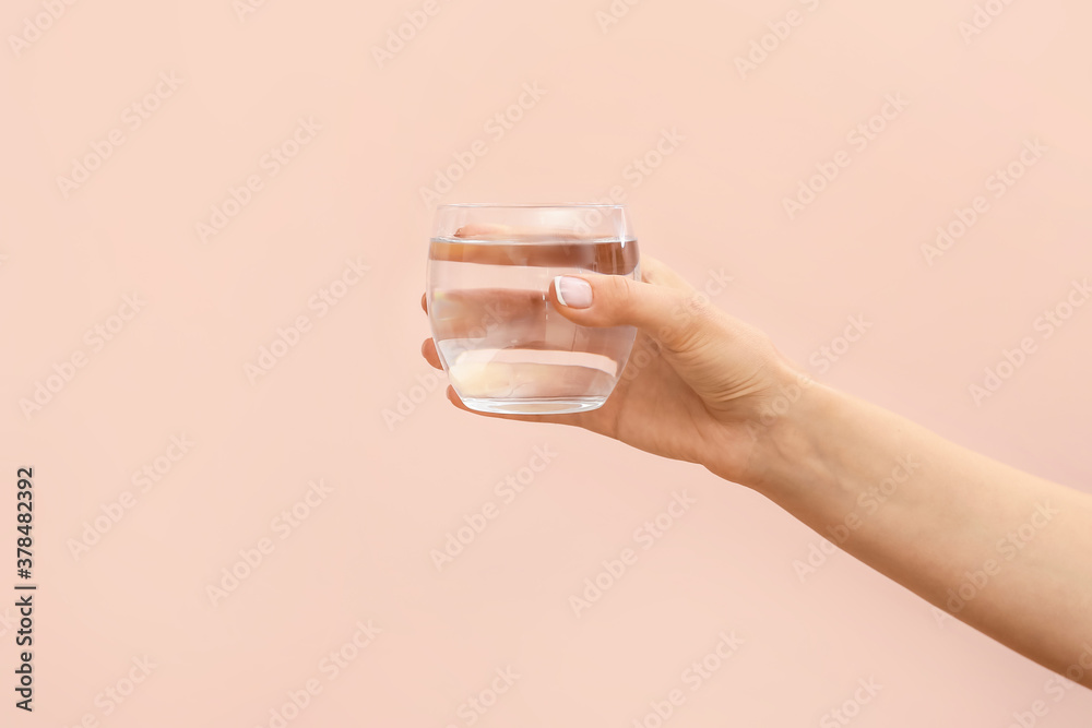 Hand with glass of water on color background