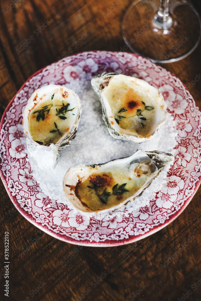 Flat-lay of oven baked oysters with parmesan cheese and herbs over sea salt in colorful plate in fis