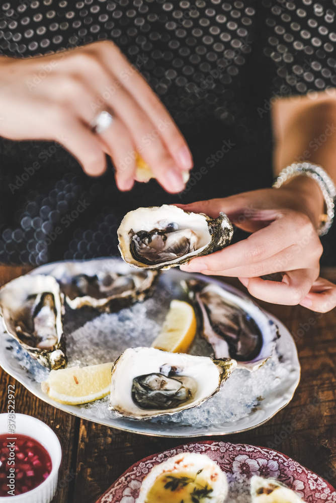 Hands of woman squeezing lemon juice to fresh Irish oysters over ice in plate in fish restaurant, se