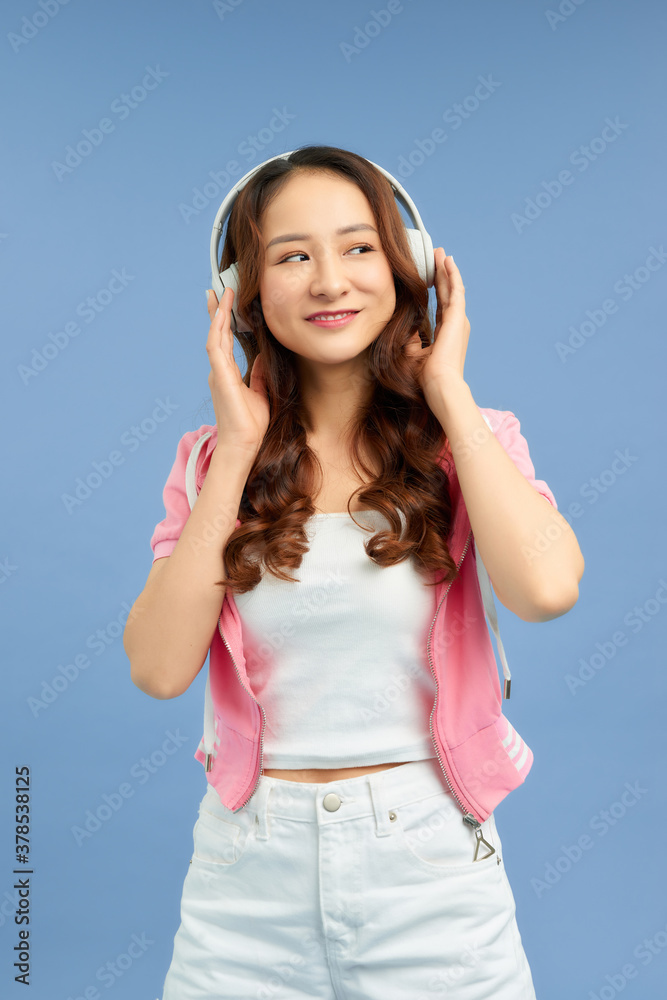 Pretty cool girl having fun and listens to music in the headphones, dancing over blue background.