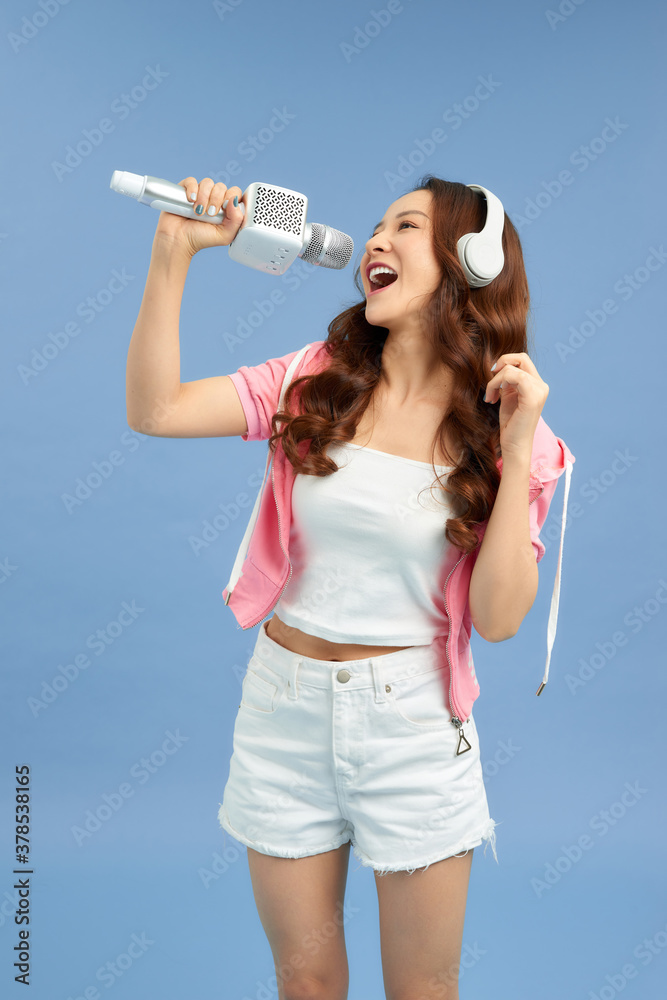 Happy young Asian woman singing with microphone sing and headphone over blue background.