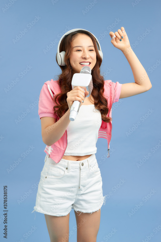 Happy young Asian woman singing with microphone sing and headphone over blue background.