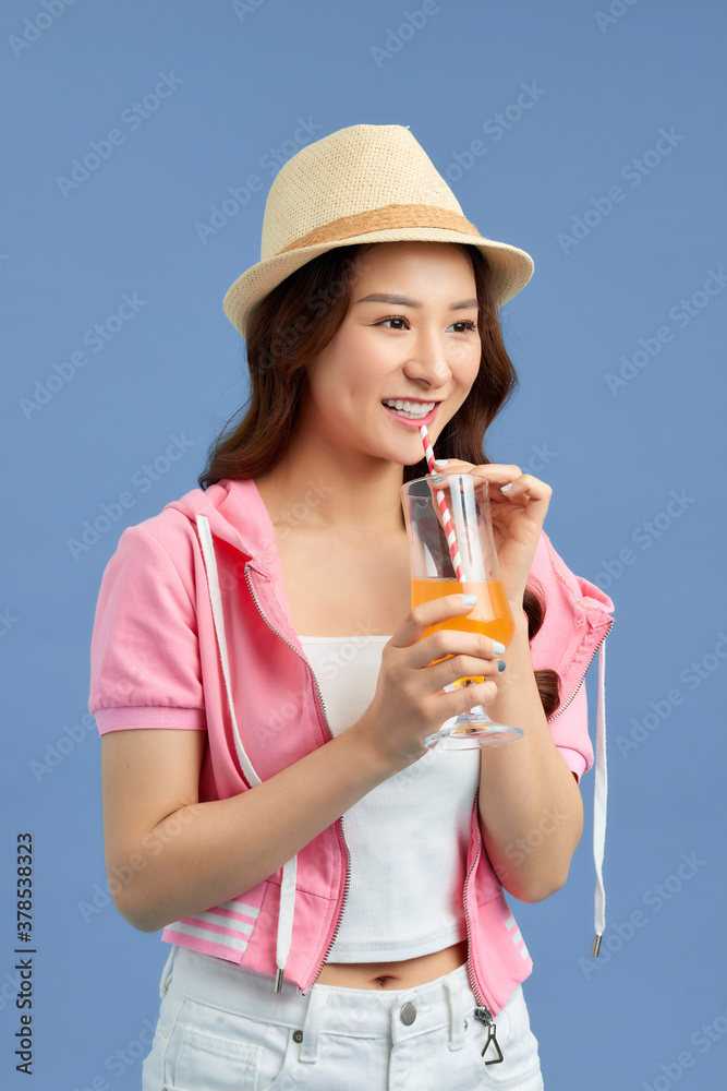 Portrait of happy young asian woman wearing straw hat and drinking fruit juice over blue background.