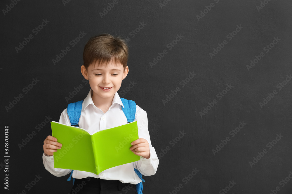 Little schoolboy with copybook on dark background