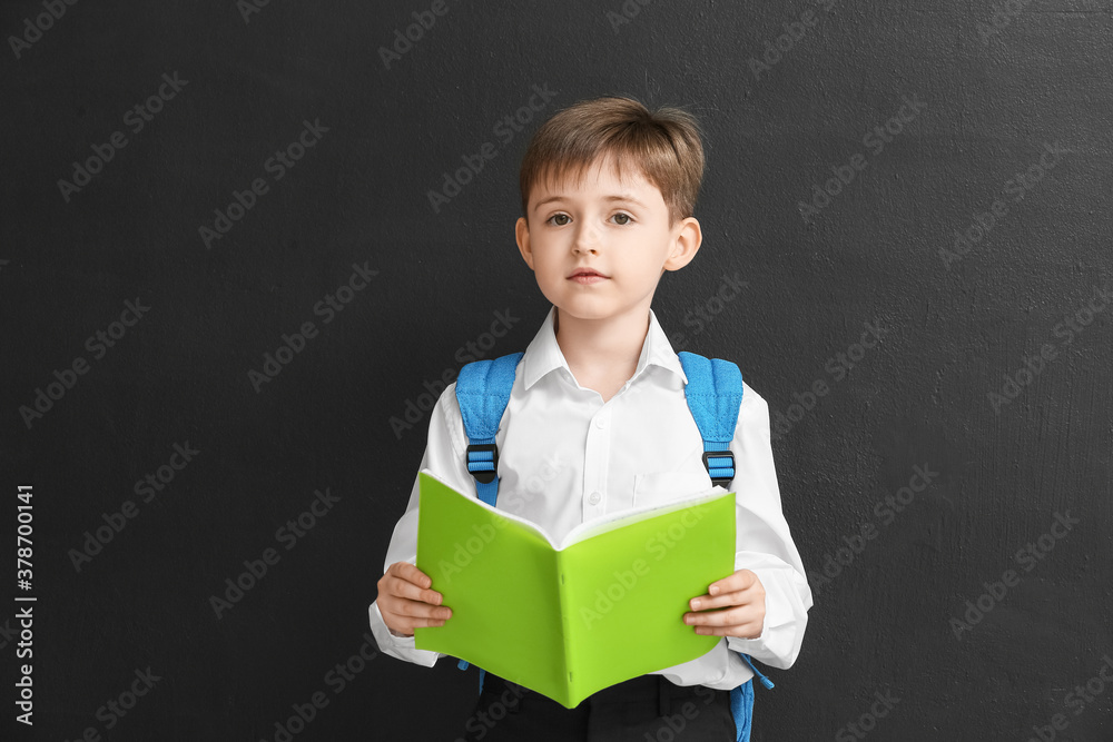 Little schoolboy with copybook on dark background