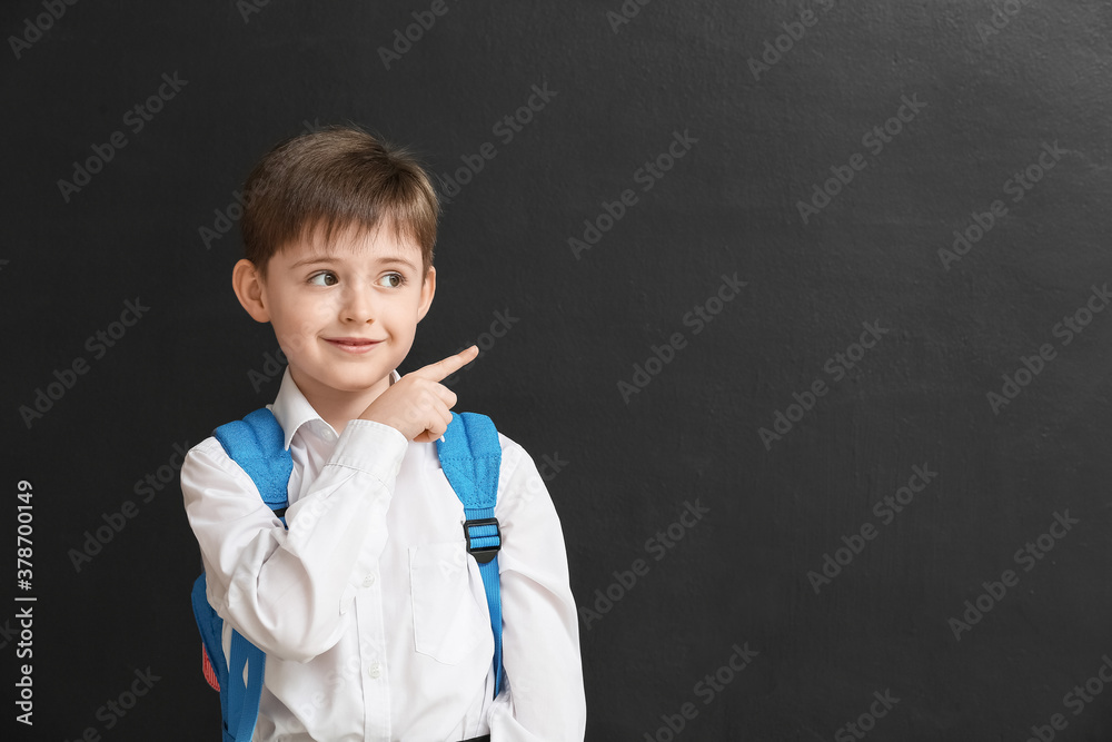 Little schoolboy pointing at something on dark background